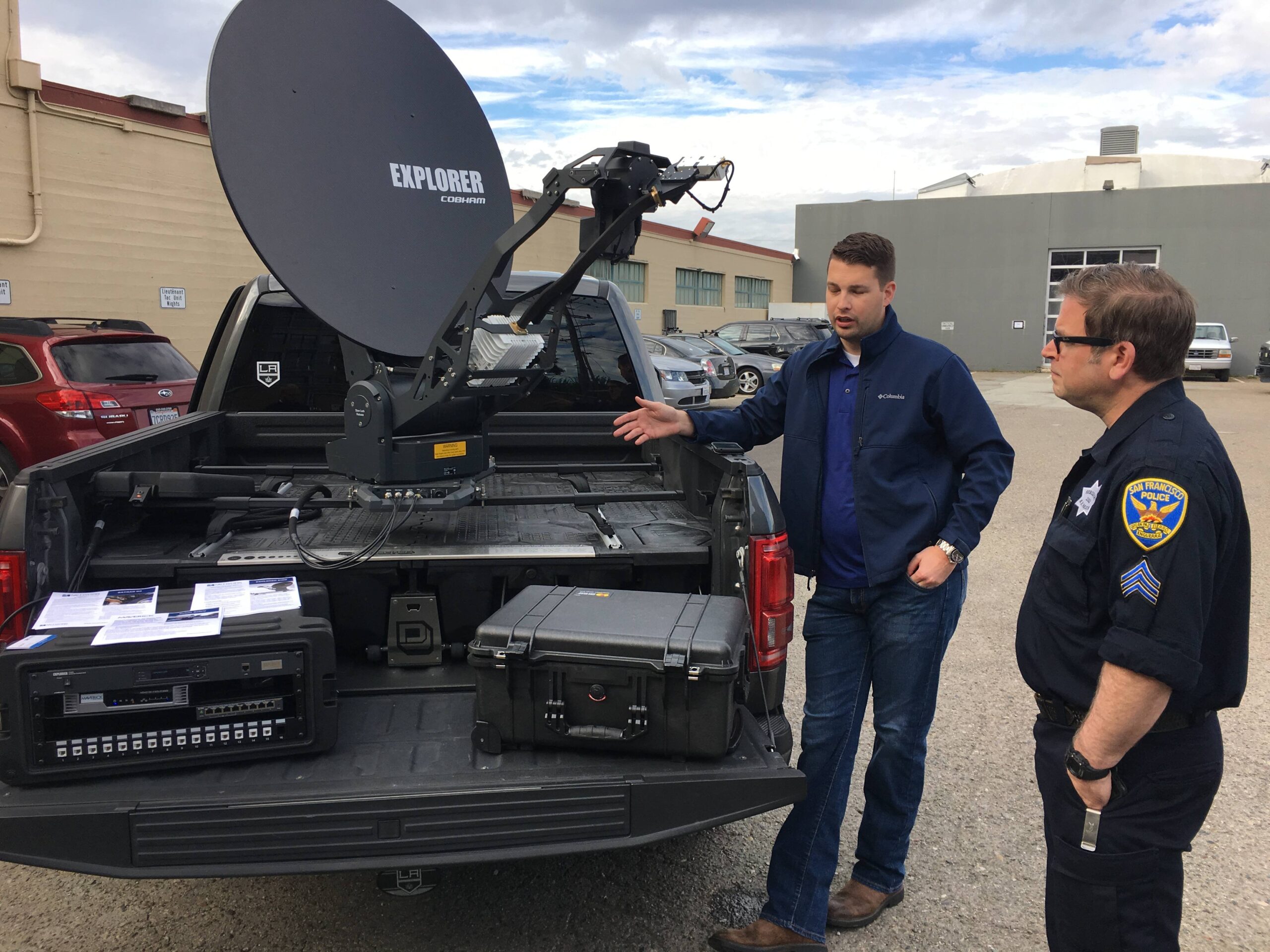 A man explaining a truckbed-mounted satellite communications system to an SFPD Sergeant